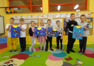 Grupa dzieci prezentuje prace plastyczne.
